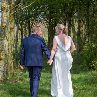Bride and groom hand in hand walking through the trees
